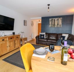 A living room with a brown leather sofa yellow chair wooden sideboard and a dining table with a bottle of wine and fruit at Pointers View in Weymouth