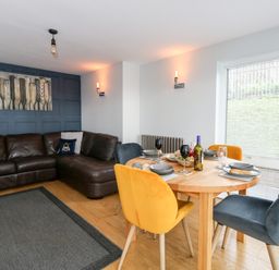 A living room with a brown leather corner sofa and a wooden dining table with colorful chairs at Pointers View in Weymouth