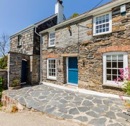Stone cottage with blue door and windows and stone patio with flowers at Mermaid Cottage in Port Isaac