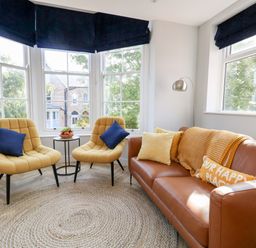 A sitting area with two yellow chairs and a brown sofa with cushions near large windows at Flat 6 Thornlow Heights Weymouth