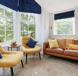 A living room with two yellow chairs with blue cushions a brown sofa with pillows and a blanket next to windows with blue blinds at Flat 6 Thornlow Heights in Weymouth