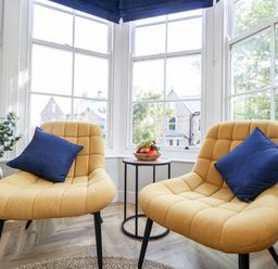 Two yellow chairs with blue pillows and a small round table with fruit between windows at Flat 6 Thornlow Heights in Weymouth