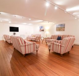 A sitting room with striped armchairs and two sofas wooden floor and TV on wall at The Old Gymnasium in Southwold