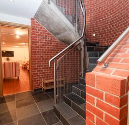 A hallway with black tiled floor red brick walls and a staircase with metal handrails at The Old Gymnasium in Southwold