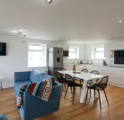 An open-plan kitchen and living area with a blue sofa a white dining table with black chairs and kitchen appliances at Treen St Ives