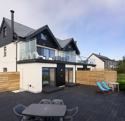 A two-story house with a balcony and outdoor seating on a wooden deck at Treen in St Ives
