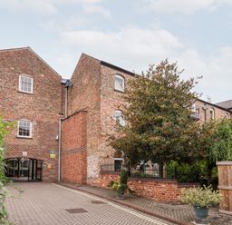 A brick building with multiple windows a gated entrance and a tree with red berries at 6 Granary Court in York