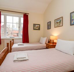 A bedroom with two single beds a wooden chest of drawers red curtains and framed pictures on the wall at 6 Granary Court in York