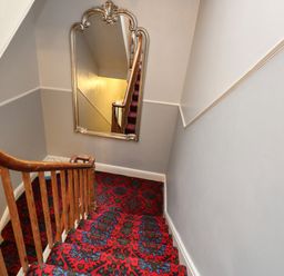 A staircase with wooden banister and red patterned carpet with a large decorative mirror on the wall at The Esplanade in Weymouth