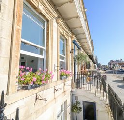 Street view of a row of buildings with flower boxes on windows and cars parked along the road at The Esplanade in Weymouth