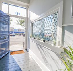 An open door with blue paint leading outside a hallway with small potted plants on a windowsill and a green plant in the corner at The Esplanade in Weymouth