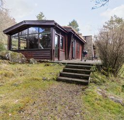A wooden cabin with large glass windows and stone steps leading to a grassy area at Rocksite in Kirkmichael Perth And Kinross