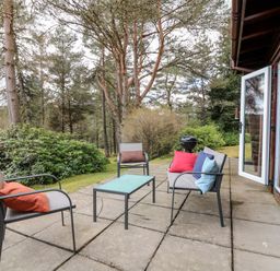 An outdoor patio with a glass table surrounded by three chairs with colorful cushions next to a wooden building at Rocksite in Kirkmichael Perth And Kinross