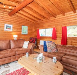 A living room with two brown sofas a wooden coffee table and red curtains at Rocksite in Kirkmichael Perth And Kinross