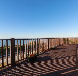 A wooden deck with railings and flower pots overlooking the sea at Sunset Sea View Chalet in Millbrook