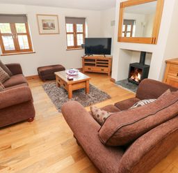 A living room with two brown sofas a wooden coffee table and a burning fireplace at Ty Melyn in Boncath