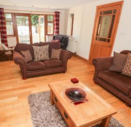 A living room with brown sofas a wooden coffee table and glass door to outside at Ty Melyn in Boncath