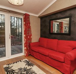 A room with a red sofa next to glass doors with red curtains and a black patterned wall with a mirror at Swinsty Lodge in Fewston near Darley