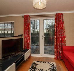 A living room with a red sofa a television on a black and white stand and glass doors with red curtains at Swinsty Lodge in Fewston near Darley