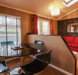 A dining area with a glass table and black chairs next to a window and a living room with a red sofa and wall mirror at Swinsty Lodge in Fewston near Darley
