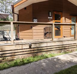 A wooden deck with outdoor furniture and umbrella beside a brown house with glass and wooden railings at Swinsty Lodge in Fewston near Darley