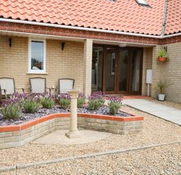 A patio area with a raised flower bed a stone pedestal and chairs at Drifters in Winterton-On-Sea