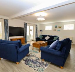 A living room with blue sofas a wooden coffee table and a wall mounted TV at Drifters in Winterton-On-Sea