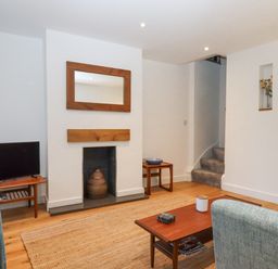 A living room with a fireplace a wooden coffee table a television and a staircase at The Cottage on The Square in Chagford