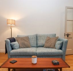 A living room with a blue sofa pillows a wooden coffee table and a floor lamp at The Cottage on The Square in Chagford