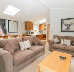 A living room with two brown sofas a wooden coffee table and a dining table with chairs at Highfield Lodge in Kirkstone 30 Limefitt Park near Troutbeck