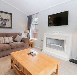 A living room with a brown sofa a wooden coffee table a wall-mounted TV and a fireplace at Highfield Lodge Kirkstone 30 Limefitt Park near Troutbeck