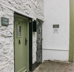 A green door numbered 12 next to a white wall with a sign reading Latch Cottage and an iron gate at Latch Cottage in Keswick