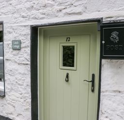 A green front door with the number 12 a black mailbox and window on a white stone wall at Latch Cottage in Keswick