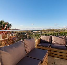 An outdoor seating area with wooden furniture and cushions overlooking a coastal landscape