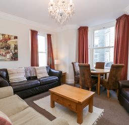 A living room with sofas a wooden coffee table and dining table with chairs at Carlton House Apartment 1 in Keswick