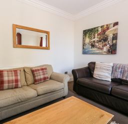 A living room with two sofas a wooden coffee table a wall mirror and a painting at Carlton House Apartment 1 in Keswick