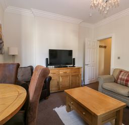 A living room with a wooden coffee table a TV on a wooden cabinet armchairs and a sofa with a plaid pillow at Carlton House Apartment 1 Keswick
