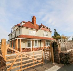 A detached two-story house with a red tiled roof behind a wooden gate and stone wall at Westholme Lodge in Minehead