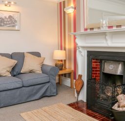 A living room with a gray sofa with beige cushions a side table with a lamp and a fireplace with firewood at Westholme Lodge in Minehead