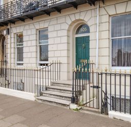 The front entrance of a beige stone building with a green door numbered 105 and black iron railings outside at Sunbeach in Weymouth
