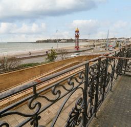 A balcony with decorative railings overlooking a road beach a clock tower and the sea at Sunbeach in Weymouth