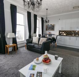 An open plan living room and kitchen with black leather sofas dining table white cabinets and large windows with black curtains at Sunbeach in Weymouth