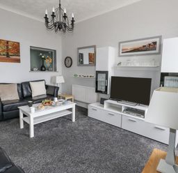 A living room with black leather sofas white coffee table with cups and food and a white TV cabinet with a television at Sunbeach Weymouth