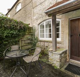An outdoor patio with a round glass table and two chairs next to a stone wall and wooden door at Field Cottage in Shepton Mallet