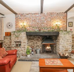 A living room with a stone fireplace red sofa wooden coffee table and a television at Field Cottage in Shepton Mallet