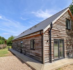 A wooden exterior of a house with multiple windows and doors next to a gravel area and trees at Lodge 24 in South Hykeham