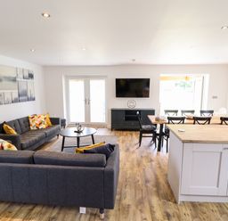 An open living room and dining area with gray sofas a round black coffee table a wooden dining table with black chairs and a TV mounted on the wall at Lodge 24 in South Hykeham