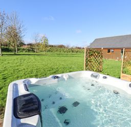 An outdoor hot tub with water in a grassy area near a wooden cabin and lattice panels at Lodge 2 in South Hykeham