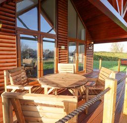A wooden outdoor deck with a round table and four chairs outside a log cabin at Lodge 4 in South Hykeham