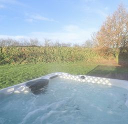 An outdoor hot tub on a wooden deck next to a grassy area with a tree at Lodge 4 in South Hykeham